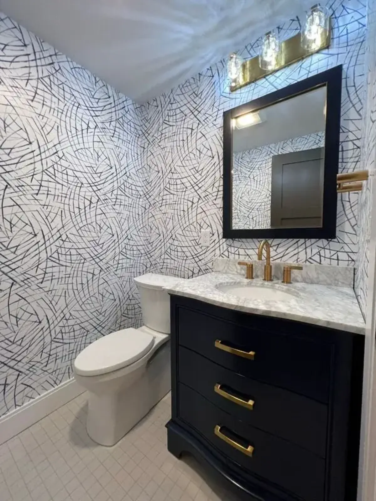 Powder room renovation in Peabody, MA with a navy vanity, marble top and brass fixtures
